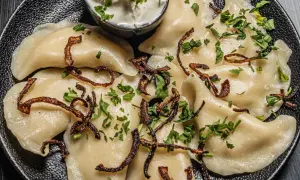 Pyszne pierogi z ziemniakami i boczkiem, posypane chrupiącą cebulką i natką pietruszki. Podane z kleksem śmietany.