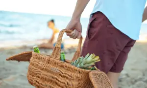 Koszyk z napojami i ananasem, idealne przekąski na plażę. W tle widać parę odpoczywającą nad morzem.