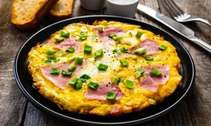 Pyszny omlet z szynką i serem, posypany szczypiorkiem, podany z grzankami. Idealny na śniadanie.