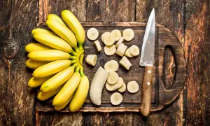 Pęczek bananów, pokrojone plasterki i nóż na drewnianej desce. Czy banany można trzymać w lodówce?
