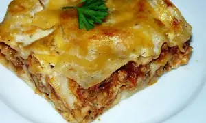 Pyszny kawałek lasagne z mięsem mielonym, zrumieniony ser i świeża natka pietruszki. Idealny przepis na obiad.