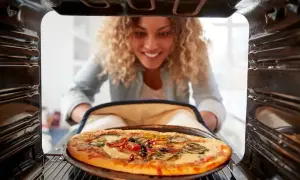 Uśmiechnięta kobieta wyjmuje z piekarnika gorącą pizzę. Idealna temperatura pieczenia pizzy to klucz do sukcesu!