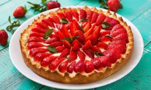 Pyszna tarta z owocami, pełna świeżych, czerwonych truskawek i listków mięty, na chrupiącym spodzie.