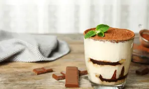 Szybki deser z niczego: kremowe tiramisu w szklance, posypane kakao i udekorowane miętą. Obok kawałki czekolady.