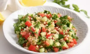 Orzeźwiająca sałatka z kaszą bulgur, pomidorami, ogórkiem i natką pietruszki, podana z cytryną.