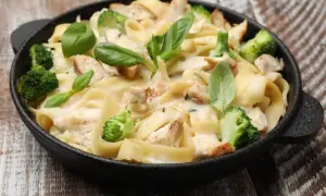 Pyszna potrawka z kurczaka z makaronem tagliatelle, brokułami i kremowym sosem, udekorowana świeżą bazylią.
