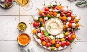 Kolorowe przystawki na zimno w kształcie wieńca, z mozzarellą, pomidorkami, oliwkami i salami, podane z dipami.