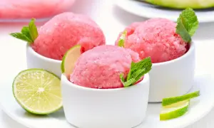 Orzeźwiający sorbet z arbuza w białych miseczkach, udekorowany listkami mięty i plasterkami limonki. Idealny na upalne dni.