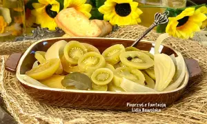 Sałatka z zielonych pomidorów z cebulą i przyprawami, podana w brązowej miseczce, na tle słoneczników.