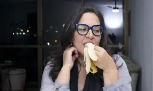 Kobieta w okularach je banana na noc, ciesząc się smakiem.