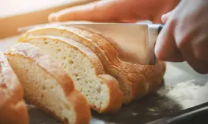Dłoń kroi świeży chleb na kromki. Dowiedz się, jak odświeżyć chleb, aby znów był pyszny.