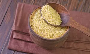 Drewniana miska pełna kaszy jaglanej, z łyżką nabierającą jej ziarna. Czy kasza jaglana ma gluten? Nie, jest bezglutenowa!