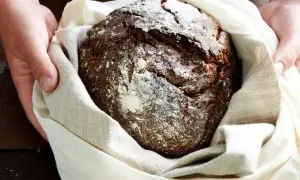 Ręce trzymają bochenek chleba żytniego, który sugeruje, jaka mąka jest najzdrowsza. Posypany mąką, zawinięty w lniany worek.
