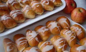 Pyszne pierogi z jabłkami, polane lukrem, kuszą swoim wyglądem. Obok leżą świeże jabłka.