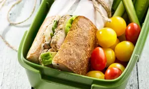 Pyszna kanapka z kurczakiem w zielonym pudełku, obok pomidorki i ogórki. Idealna na lunch!