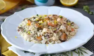 Pyszne risotto z owocami morza, udekorowane skórką cytrynową i ziołami, na białym talerzu.
