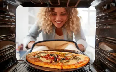 Uśmiechnięta kobieta wyjmuje z piekarnika gorącą pizzę. Idealna temperatura pieczenia pizzy to klucz do sukcesu!