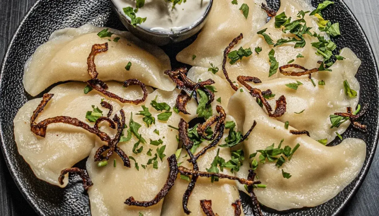 Pyszne pierogi z ziemniakami i boczkiem, posypane chrupiącą cebulką i natką pietruszki. Podane z kleksem śmietany.