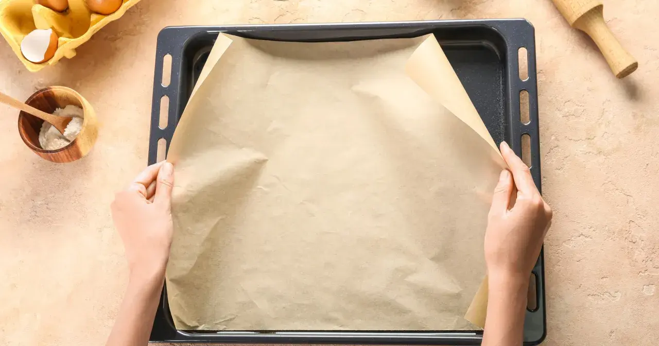 Ręce układają papier do pieczenia na blasze. Zastanawiasz się, czym zastąpić papier do pieczenia? Masz już składniki do ciasta.