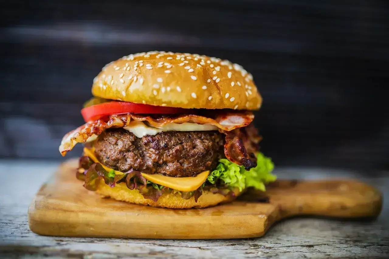 Soczysty burger z wołowiny, idealne mięso na burgery, z bekonem, serem i warzywami na desce.