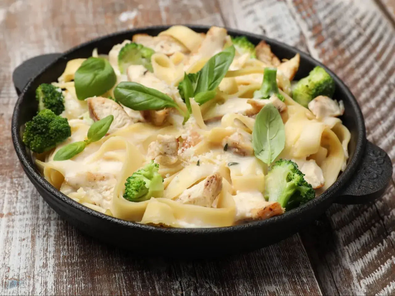 Pyszna potrawka z kurczaka z makaronem tagliatelle, brokułami i kremowym sosem, udekorowana świeżą bazylią.