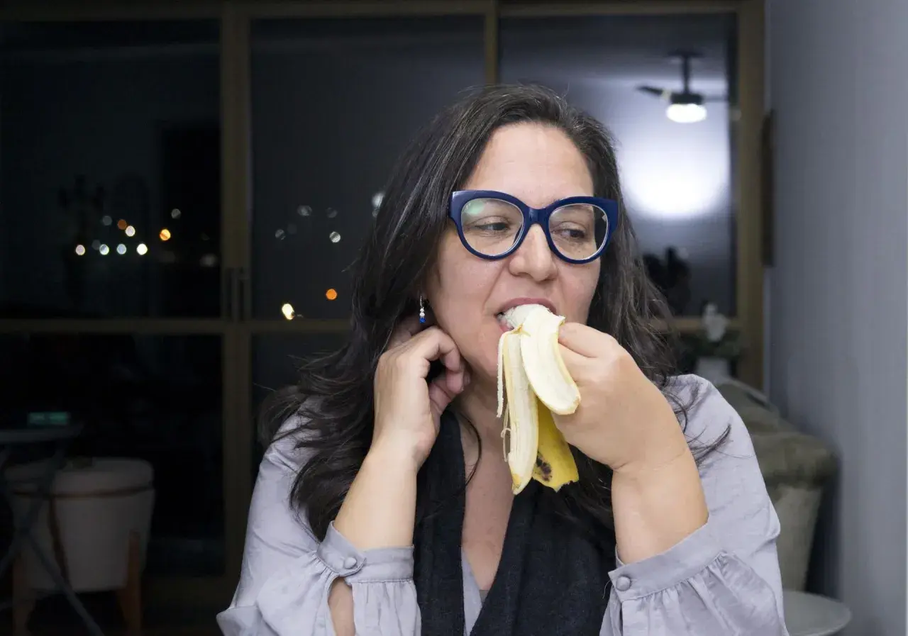 Kobieta w okularach je banana na noc, ciesząc się smakiem.