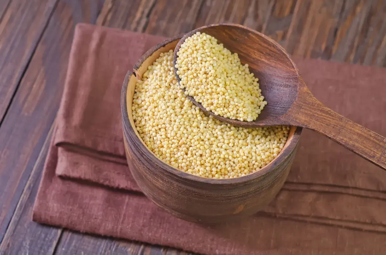 Drewniana miska pełna kaszy jaglanej, z łyżką nabierającą jej ziarna. Czy kasza jaglana ma gluten? Nie, jest bezglutenowa!