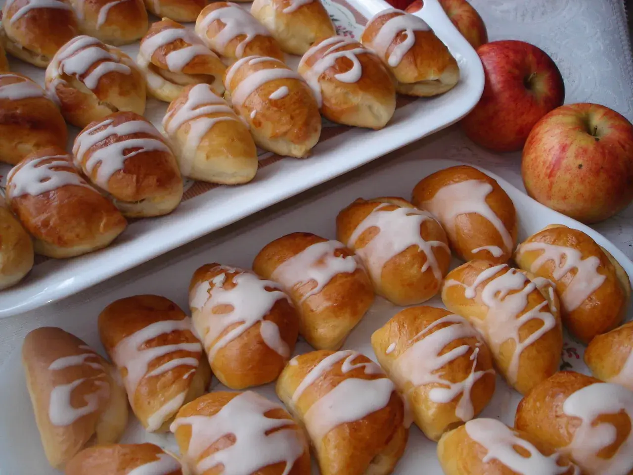 Pyszne pierogi z jabłkami, polane lukrem, kuszą swoim wyglądem. Obok leżą świeże jabłka.