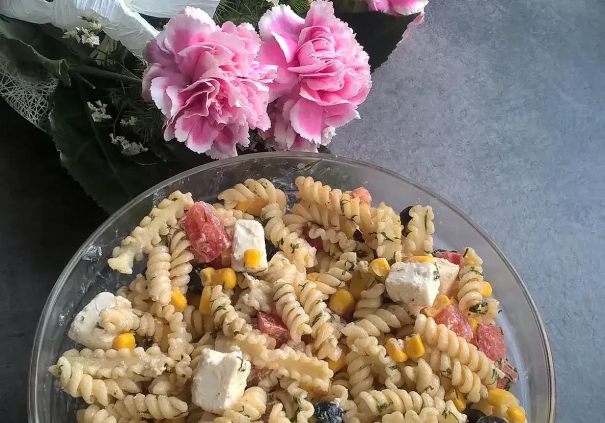 Pyszna sałatka z makaronem fusilli z fetą, pomidorkami i kukurydzą, ozdobiona r&oacute;żowymi kwiatami.