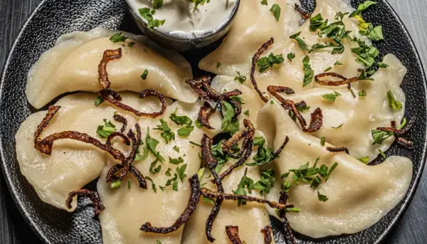 Pyszne pierogi z ziemniakami i boczkiem, posypane chrupiącą cebulką i natką pietruszki. Podane z kleksem śmietany.