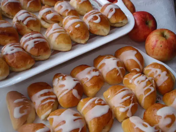 Pyszne pierogi z jabłkami, polane lukrem, kuszą swoim wyglądem. Obok leżą świeże jabłka.