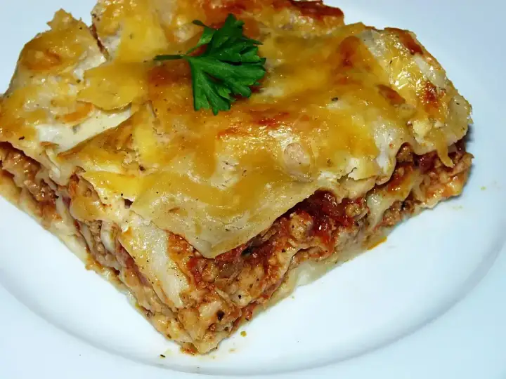Pyszny kawałek lasagne z mięsem mielonym, zrumieniony ser i świeża natka pietruszki. Idealny przepis na obiad.